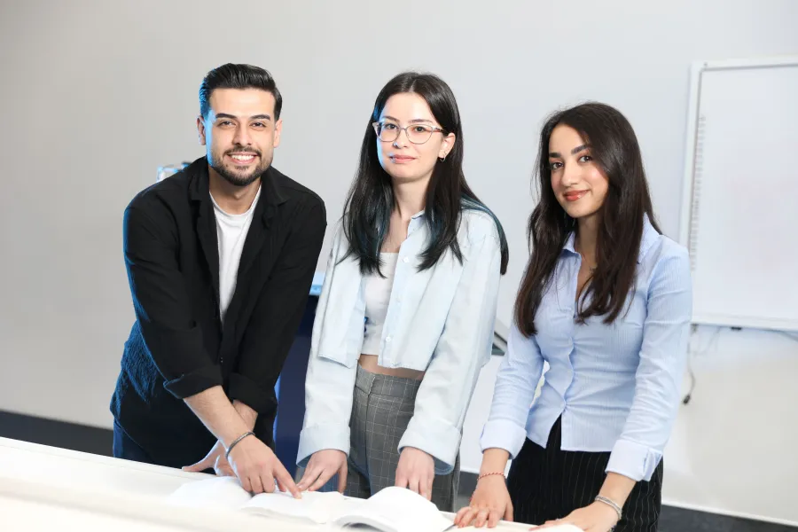 Trois étudiants en tenue professionnelle autour d'un document, en salle de cours